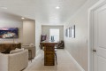 Basement recreation room with a wooden bar, two beige armchairs, and a wall-mounted TV showing an outdoor scene, plus framed photos on the right wall.