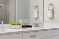 White bathroom counter with a planter of succulents, a small sign about makeup towels, and a tray with black rolled towels beside a brushed-metal faucet.