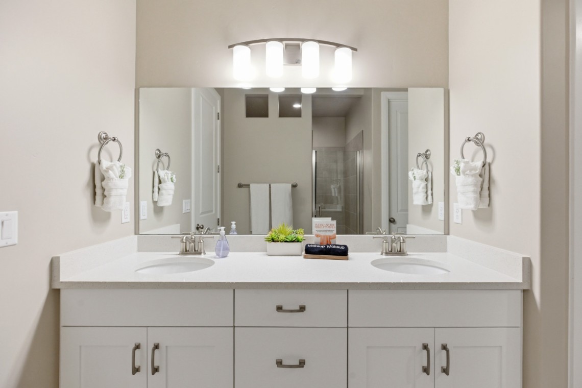 Double-sink bathroom vanity with white countertop, mirrored wall, and four-light fixture above