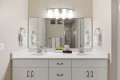 Double-sink bathroom vanity with white countertop, mirrored wall, and four-light fixture above
