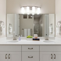 Double-sink bathroom vanity with white countertop, mirrored wall, and four-light fixture above