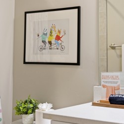 Framed colorful animal illustration on a gray bathroom wall, with a polka-dot shower curtain on the left and a white countertop with decor on the right.