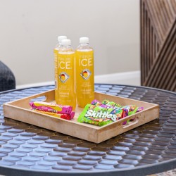 Wooden tray on a round metal table holding two Sparkling ICE bottles and Skittles candy bars on an outdoor patio table.