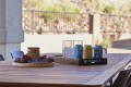 Outdoor patio table with a tray of colorful soda cans and a glass ice bucket, plus a jar of salsa and chips on a round board (snack setup).