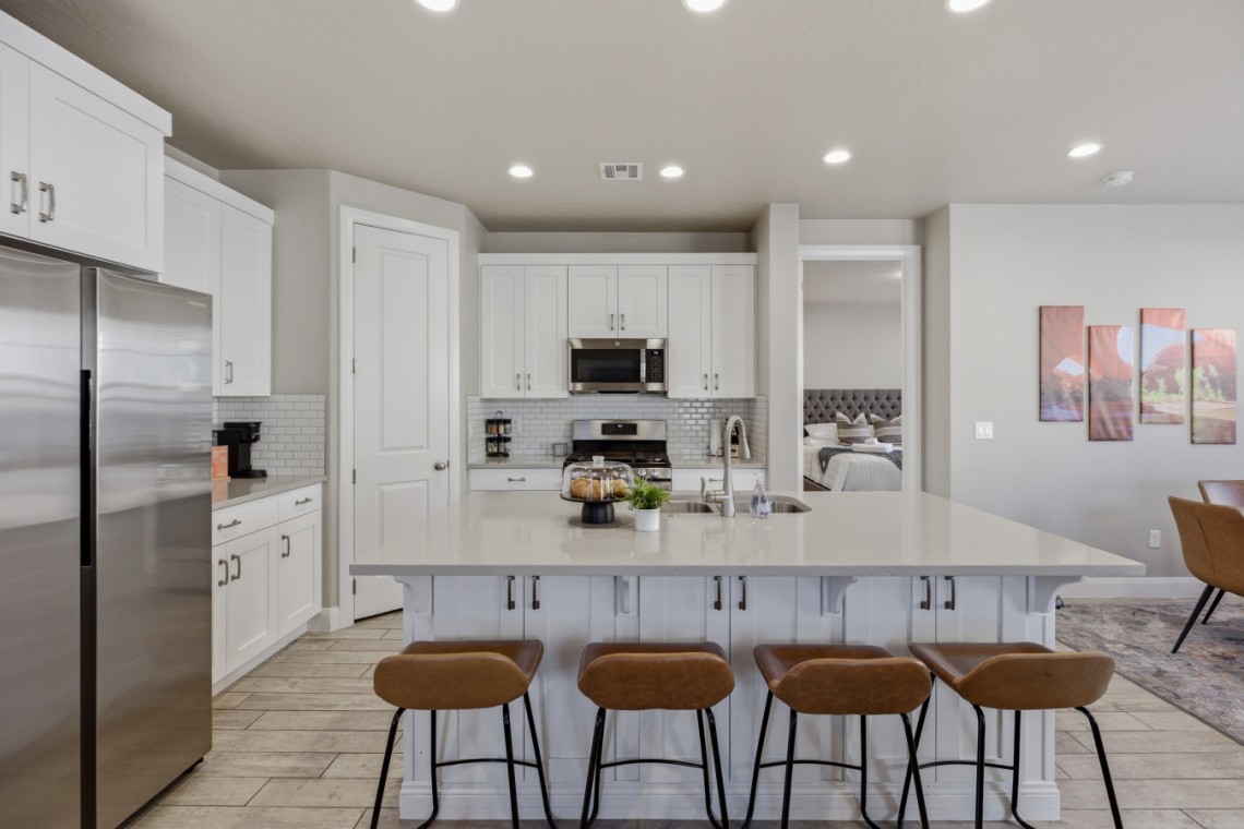 Modern kitchen with white cabinets, stainless steel fridge, and a large white island with four brown bar stools.