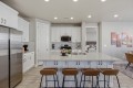 Modern kitchen with white cabinets, stainless steel fridge, and a large white island with four brown bar stools.