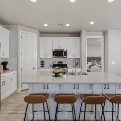 Modern kitchen with white cabinets, stainless steel fridge, and a large white island with four brown bar stools.