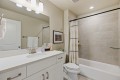 Modern bathroom with a white vanity, large mirror, and beige tiled shower/ tub area.