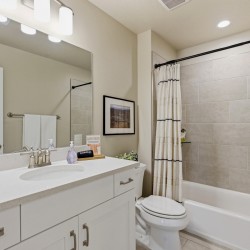 Modern bathroom with a white vanity, large mirror, and beige tiled shower/ tub area.