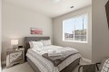 Gray upholstered bed with patterned bedding, gray throw, and folded towels on a nightstand in a bright bedroom.