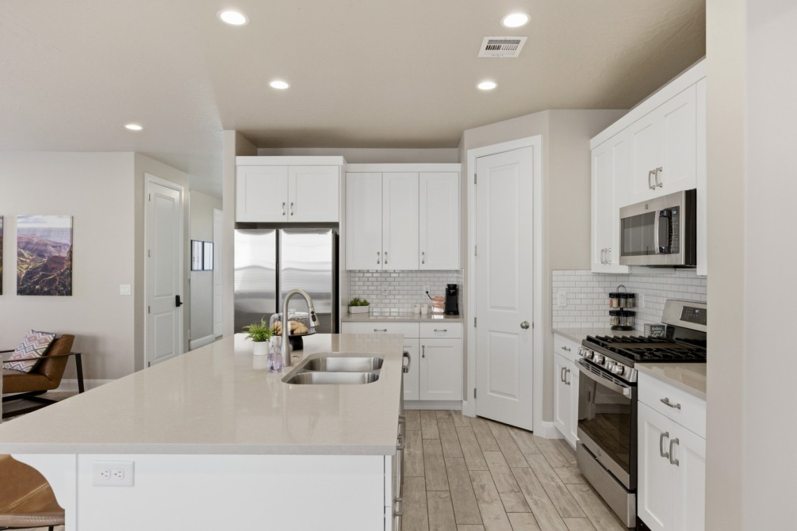 Bright white kitchen with an island, double sink, and stainless steel fridge and appliances.