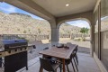 Covered patio with a wooden dining table and eight chairs, a gas grill on the left, and desert hills in the background.