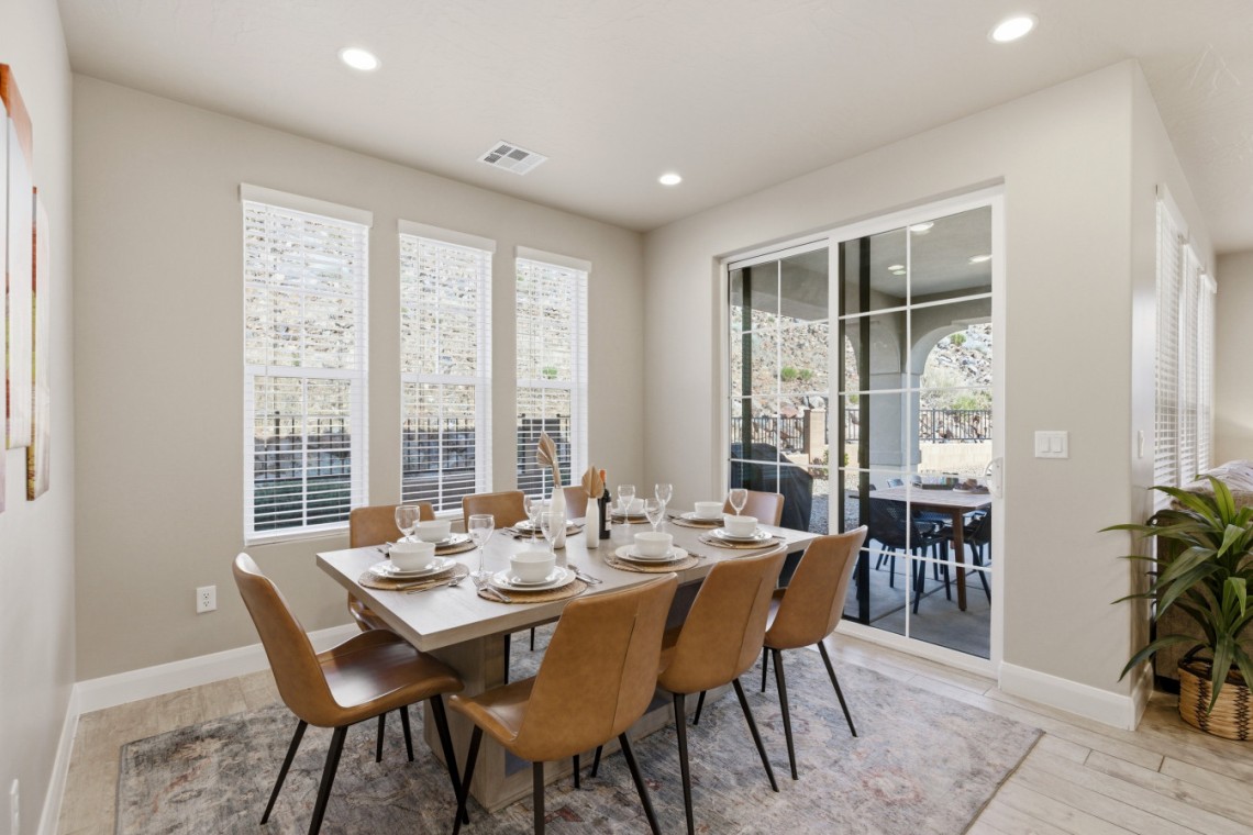Dining room with a wooden table set for eight, tan chairs, and a sliding glass door to a patio outdoor seating area.