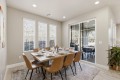 Dining room with a wooden table set for eight, tan chairs, and a sliding glass door to a patio outdoor seating area.