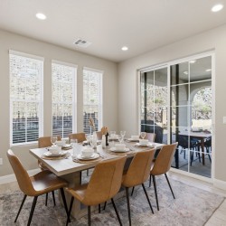 Dining room with a wooden table set for eight, tan chairs, and a sliding glass door to a patio outdoor seating area.