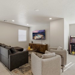 Cozy basement living area with a dark gray sectional, two beige chairs, and a mounted TV above a wooden cabinet.