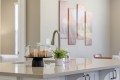 Croissants under a glass cake dome on a white kitchen island with a small potted plant nearby and a modern faucet in the background.