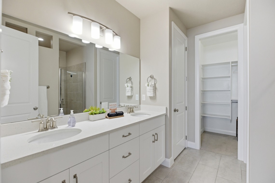 Bright modern bathroom with a double vanity, white cabinetry, and a large illuminated mirror above two sinks.