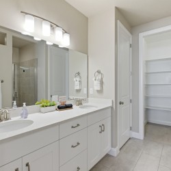 Bright modern bathroom with a double vanity, white cabinetry, and a large illuminated mirror above two sinks.