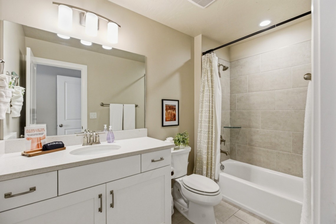 A modern bathroom with a white vanity, large mirror, and sink; toilet beside a bathtub with a patterned shower curtain.