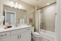A modern bathroom with a white vanity, large mirror, and sink; toilet beside a bathtub with a patterned shower curtain.
