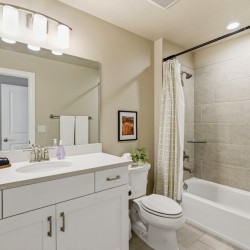 A modern bathroom with a white vanity, large mirror, and sink; toilet beside a bathtub with a patterned shower curtain.