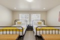 Twin bedroom with two metal-framed beds, white linens, and yellow knit throws, centered by a shared nightstand and lamp.