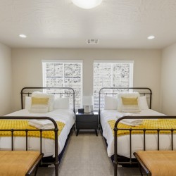 Twin bedroom with two metal-framed beds, white linens, and yellow knit throws, centered by a shared nightstand and lamp.