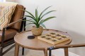 Round wooden coffee table with a green plant in a woven basket and a wooden grid-style game beside a brown leather chair.