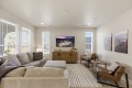 Bright living room with a beige sectional, striped rug, two brown armchairs, and a wall-mounted TV above a wooden console.