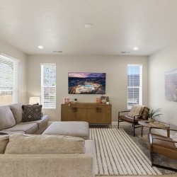 Bright living room with a beige sectional, striped rug, two brown armchairs, and a wall-mounted TV above a wooden console.