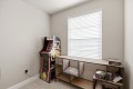A small game corner with a vintage arcade cabinet beside a long wooden desk and shelving under a window with white blinds.