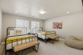 Two twin metal-frame beds with white linens and bright yellow knit throws, matching benches at the foot, in a neutral-lit bedroom with two windows and a landscape print on the wall.