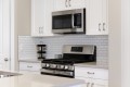 Stainless steel microwave above a gas range in a white kitchen with a subway tile backsplash.