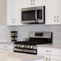 Stainless steel microwave above a gas range in a white kitchen with a subway tile backsplash.