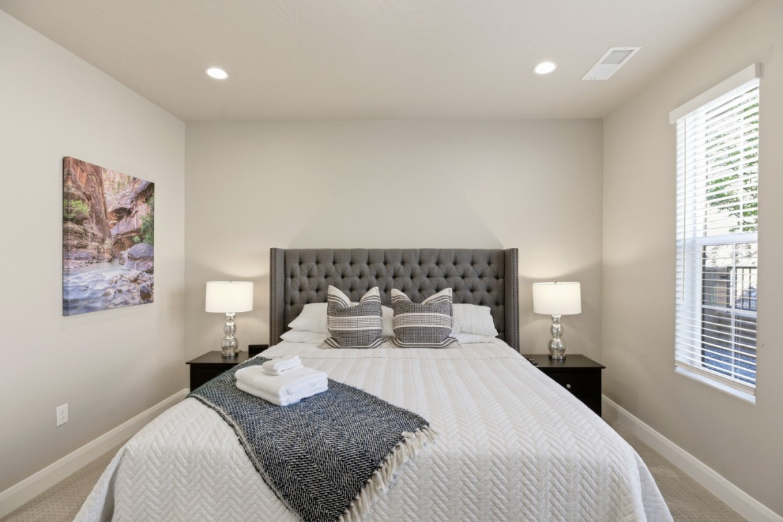 Bedroom with a gray tufted headboard, two nightstands with lamps, and a window with blinds on the right.
