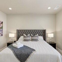 Bedroom with a gray tufted headboard, two nightstands with lamps, and a window with blinds on the right.