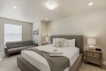 Hotel-style bedroom with a gray upholstered king bed, matching headboard, two nightstands, and a gray sofa against the wall at left.