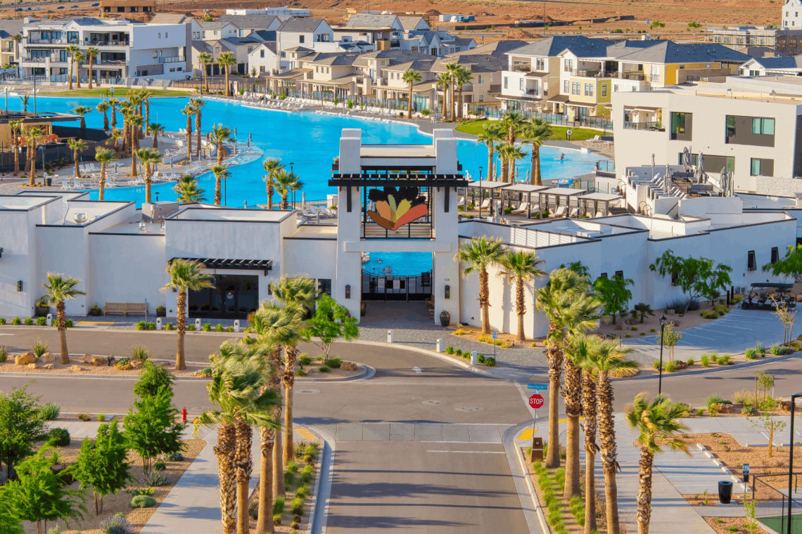 A resort complex with a large blue pool, white modern buildings, and tall palm trees surrounding the area.