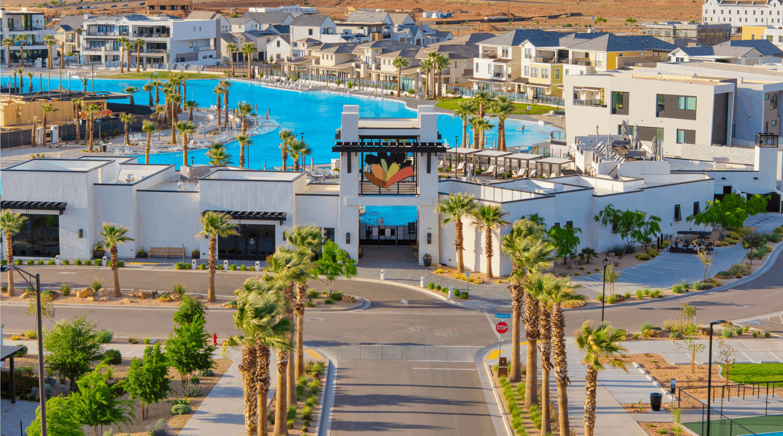 A resort complex with a large blue pool, white modern buildings, and tall palm trees surrounding the area.