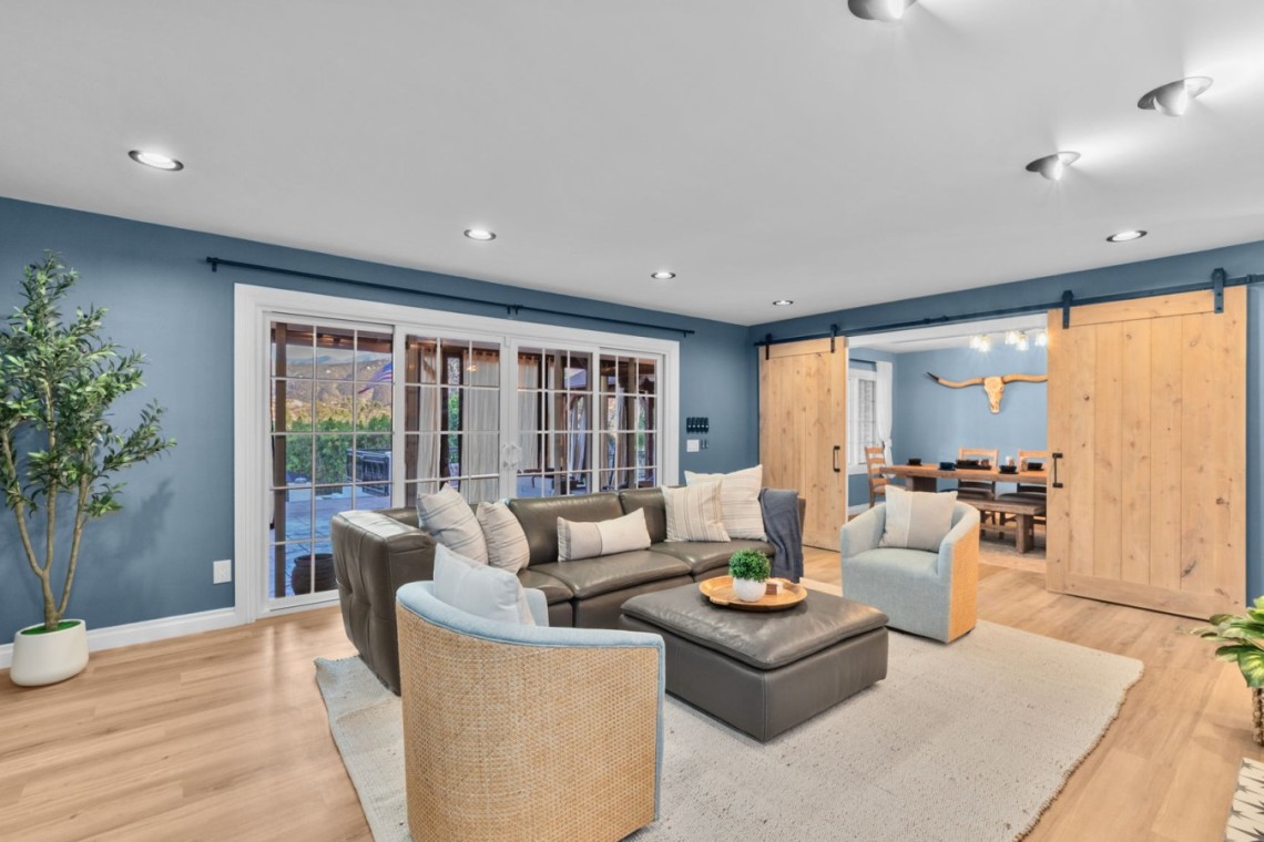 Spacious living room with blue walls, a black leather sectional, two woven chairs, and a beige rug, plus sliding barn doors to a dining area.
