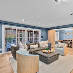 Spacious living room with blue walls, a black leather sectional, two woven chairs, and a beige rug, plus sliding barn doors to a dining area.
