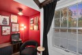 Cozy red-walled listening nook with a turntable on a wooden cabinet, framed vinyl posters, and a black curved chair by a large window with dark curtains.