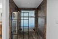 Walk-in shower with a black-framed glass door, dark stone walls, and a frosted window; a few bottles sit on the shower ledge/corner shelf.