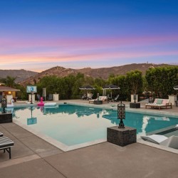 Luxurious outdoor pool area at dusk with striped lounge chairs, umbrellas, and mountain backdrop.