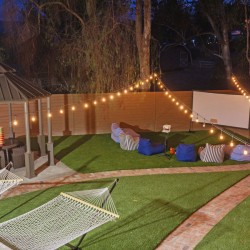 Nighttime backyard party setup with string lights, a central gazebo, hammocks, and a projector screen.