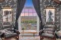 Cozy seating area with two black leather chairs facing a large window showing a sunset over a patio, framed horse and figure portraits, and horse-themed wallpaper.