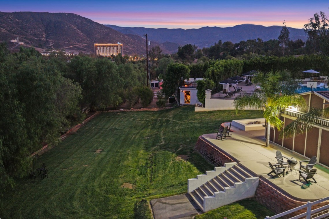 Resort lawn and terrace at dusk with palm trees, chairs, and a pool visible on the right, mountain backdrop.