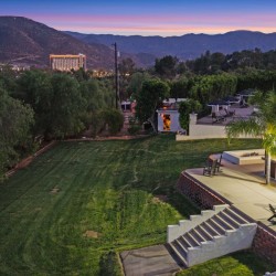 Resort lawn and terrace at dusk with palm trees, chairs, and a pool visible on the right, mountain backdrop.