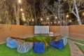 Outdoor backyard movie setup at night with a white projection screen, projector on a stand, string lights overhead, and blue and striped bean bag chairs on artificial turf.